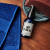 Blue bottle of 'My Beard Oil' with a blue towel and comb on a wooden surface